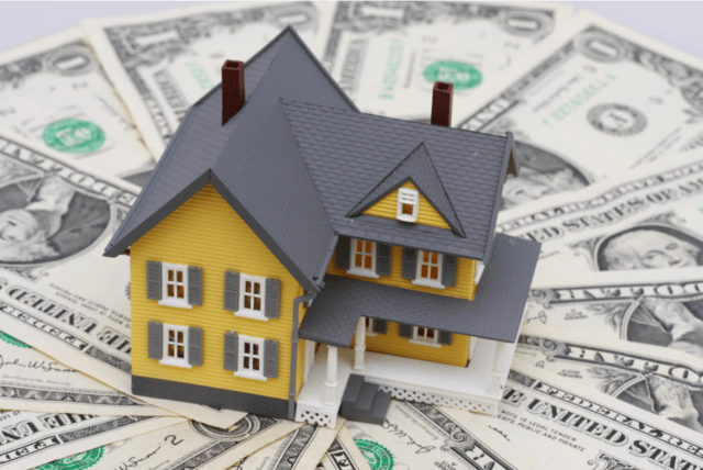 Model home placed on U.S. dollar bills, representing real estate financing, mortgage lending, or home investment.